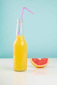橘子饮料和西柚片在白色和蓝色背景。 柑橘果汁瓶和水果在稀疏明亮环境下的极简形象。