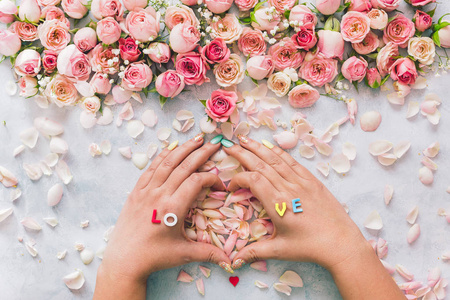 女性用双手围绕玫瑰背景的花瓣制作爱情心形。 平铺设计