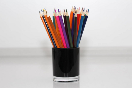 学童和学生用彩色铅笔。 铅笔散落在一张白色的桌子上，站在玻璃里。 上班族的铅笔。