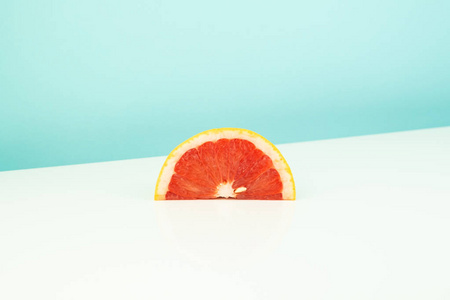 白色和蓝色背景上的一块柚子。 稀疏明亮环境下柑橘切片的极简主义图像。