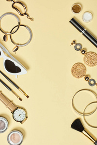 手表太阳镜，眼影，化妆品刷，手镯，耳环，睫毛膏，黄色背景