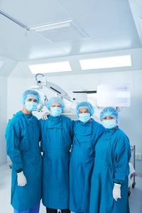四位医生身着制服，相互拥抱，一边看着摄像机，一边站在现代医院的手术室里