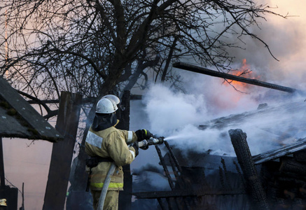 消防员灭火..消防人员用水拿着软管，在浓烟中浇灌燃烧的木结构。