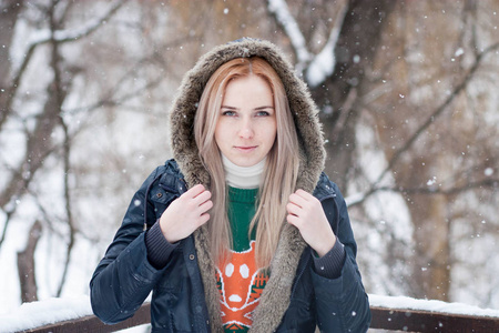 一个美丽而富有表现力的年轻女孩，长着一头金色的长发，在一个白雪皑皑的冬季公园的模糊背景