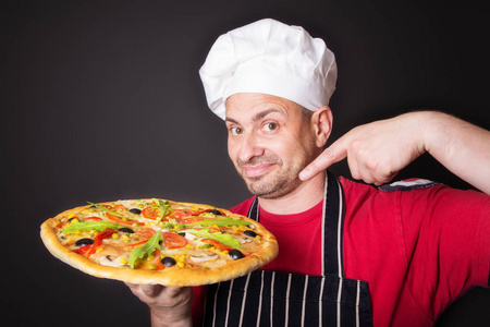一个黑色背景的工作室里有一个披萨的快乐迷人的厨师的肖像。
