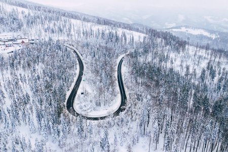 弯曲多风的道路在积雪覆盖的森林自上而下的鸟瞰。 冬季景观。