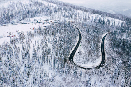 弯曲多风的道路在积雪覆盖的森林自上而下的鸟瞰。 冬季景观。