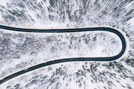 弯曲多风的道路在积雪覆盖的森林自上而下的鸟瞰。 冬季景观。