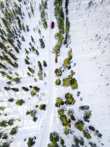 鸟瞰红色汽车驾驶通过白色雪冬林在芬兰拉普兰乡村道路。 无人驾驶飞机的俯视图