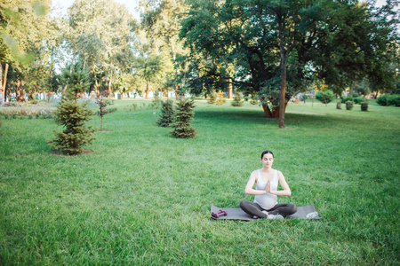 平静祥和的孕妇独自坐在公园外的莲花姿势。她双手合拢, 祈祷。模特看起来平静而平静