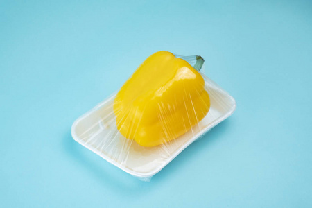 钟椒包裹在蓝色背景的塑料保鲜膜中.摄影图