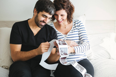 快乐而兴奋的怀孕夫妇看着他们的孩子坐在床上的超声波图像