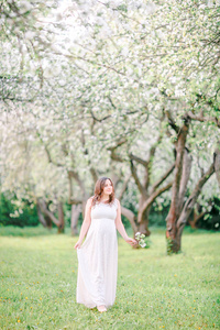 穿着白衣的怀孕少女微笑着走在苹果园