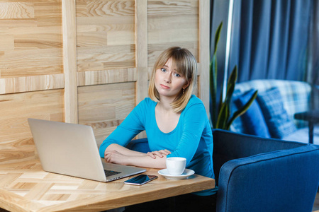 一个穿蓝色衬衫的自由职业者独自坐在咖啡馆里，在笔记本电脑上寻找工作