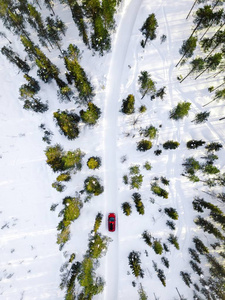 鸟瞰红色汽车驾驶通过白色雪冬林在芬兰拉普兰乡村道路。 无人驾驶飞机的俯视图