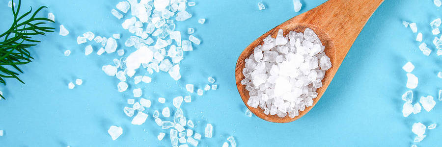 大海盐的水晶放在一个木勺里，在一张蓝色的桌子上