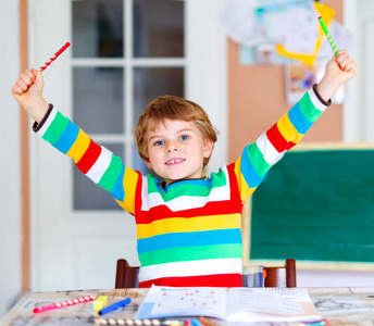 肖像的可爱快乐的学校孩子男孩在家里做家庭作业。用彩色铅笔，在屋里写字的小孩。小学和教育
