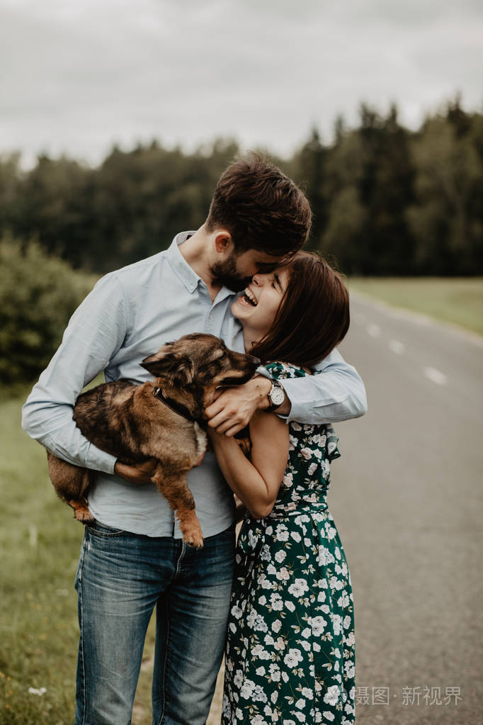 一对相爱的年轻夫妇在绿茵场上拥抱狗的画像照片-正版商用图片1887rf