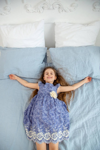 一个明亮房间里快乐的小女孩躺在床上。 假期的好心情。