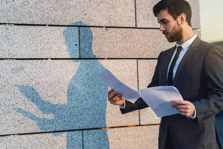 阳光下的阴影用经典的西装把严肃的年轻商人关起来,以纸的形式阅读有