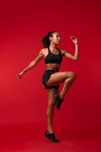 一个强壮的年轻非洲运动健身妇女的形象，摆在红墙背景上，做运动。