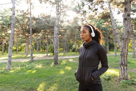 穿着黑色运动服和耳机穿过绿色公园的20多岁年轻女子的形象