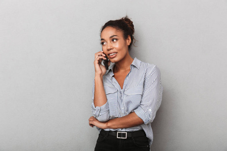 自信的非洲商务女性穿着衬衫，站在灰色的一边，用手机交谈