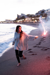 年轻快乐的微笑女子，手持燃烧的孟加拉灯站在海边