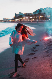 年轻快乐的微笑女子，手持燃烧的孟加拉灯站在海边