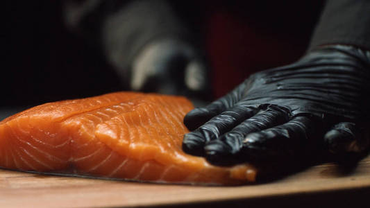 特写镜头的厨师与红三文鱼片。戴黑色手套的专业厨师拿着一块新鲜的三文鱼, 准备切它