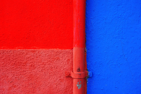 一座典型的博拉诺岛房子的墙被分成两半，涂上了明亮的红色和蓝色。 背景。