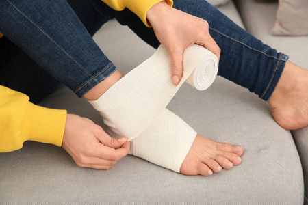 年轻女子在家中特写时用绷带包扎受伤的腿。 急救