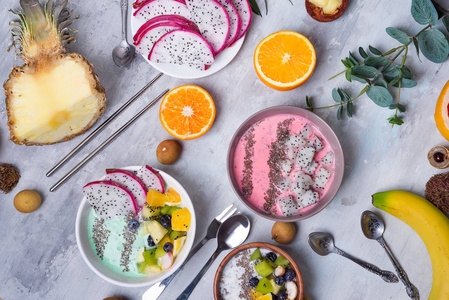 早餐桌上有酸奶阿凯碗和新鲜的热带水果，背景是灰色的石头和桉树叶。
