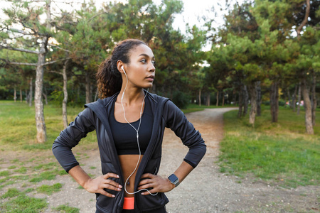 20岁左右的健康女性穿着黑色运动服和耳机绿色公园跑步时锻炼身体的形象