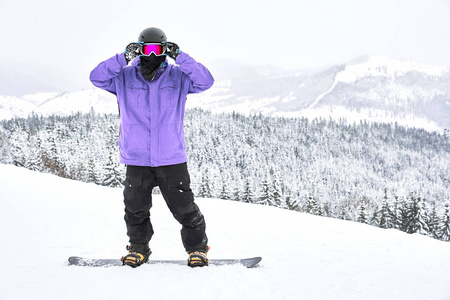 滑雪者站在他的滑雪板上，拉直谷歌在他面前，他背后有着惊人的山和木景观