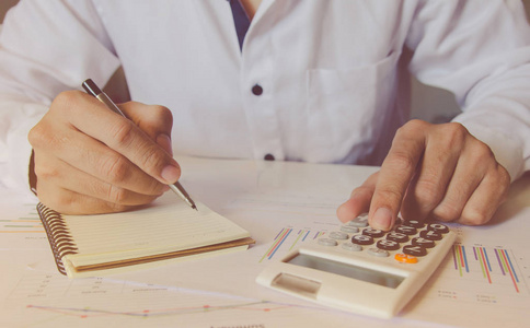 一个人用一个带笔记的财务计算器，在家里的办公桌上分析财务数据