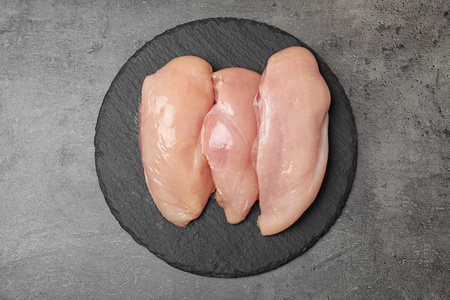 石板板与生鸡胸在灰色背景顶部视图。 新鲜肉