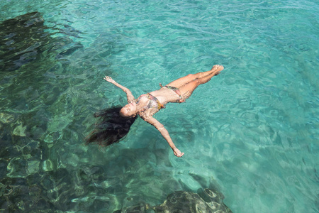 迷人的混赛女子在比基尼躺在透明的蓝色水在热带岛屿海滩。巴厘岛, 印度尼西亚