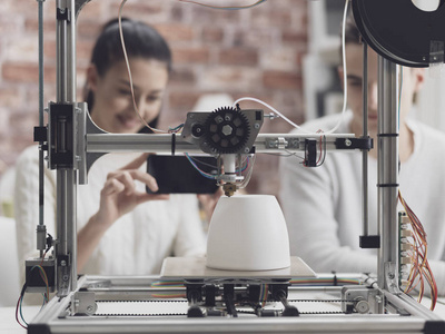 工程系学生使用3D打印机打印原型模型，女孩正在用智能手机拍照，并在网上分享