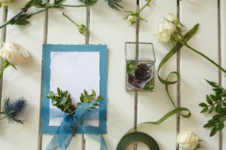 新鲜的白玫瑰和白色木桌上的结婚邀请卡。 活动鲜花装饰。 花店工作流程。 婚宴设计。