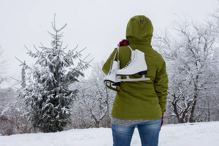 穿着绿色夹克和冰鞋的女人看着雪林