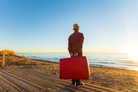旅行,假期和夏季概念--日落时拿着行李箱的人的背影照片