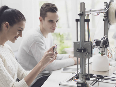 工程系学生使用3D打印机打印原型模型，女孩正在用智能手机拍照，并在网上分享