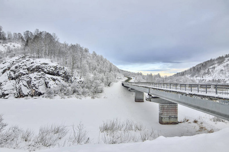 公路与桥梁穿过雪山悬崖，美丽的冬季黄昏景观。 白桦树和松林在山坡上，用海霜覆盖在道路上，冬天的旅行者