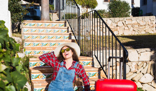 旅行旅游情感和人的概念快乐的年轻女子坐在楼梯上, 戴着红色手提箱的帽子