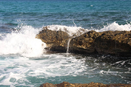 海浪拍打在岸边的一块大石头上，白色的飞溅，清澈的大海，海上度假