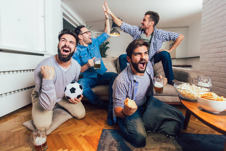 男人一起在电视上看运动，在家尖叫欢快。 一群朋友坐在沙发上看足球比赛。
