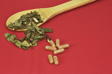 绿茶叶和胶囊放在一个用竹子做的红色背景的木勺里.照片
