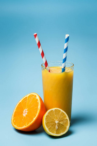 一杯新鲜的朱丝和两个纸管，旁边是柠檬和一个蓝色背景的橘子