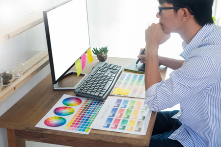 设计师编辑在工作绘图草图一个新的项目，在图形平板电脑和调色板坐在办公桌上与电脑在工作室或办公室。
